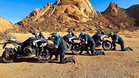 The three riders on the Indian men’s team kneeling in front of their motorcycles.